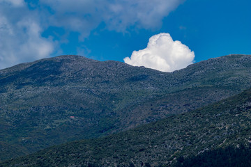 White puffy cloud pops out from behind the mountain peaks near the town of Ioannina, Greece