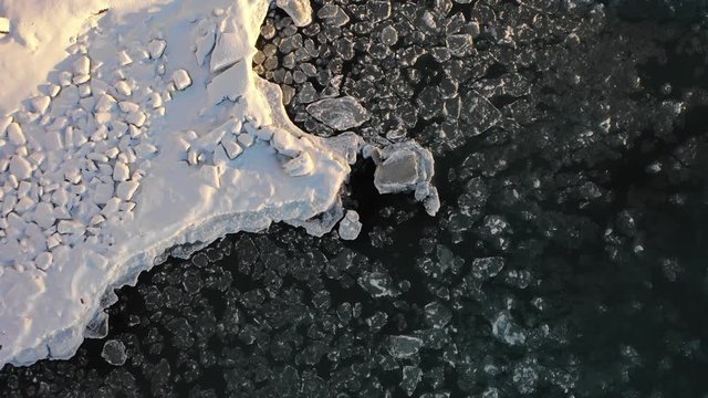 Aerial footage of abstract pattern of floating ice floes released from a waterfall in Winter season, whirlpool like effect in river Iceland