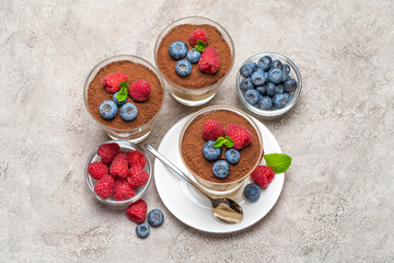 Obraz na płótnie Canvas Classic tiramisu dessert with blueberries and raspberries in a glass and bowls with berries on concrete background
