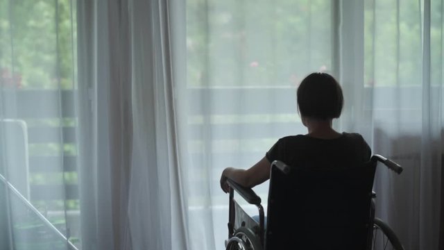 Depressed sad woman in worn wheelchair looking out the window