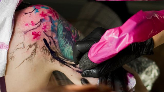 Girl makes a tattoo on his shoulder in a tattoo parlor