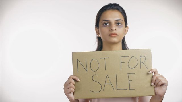 Bruised Indian woman showing 'not for sale' sign broad - human trafficking concept. Young female victim of human trafficking holding a placard of 'not for sale' text  telling the world that human i...