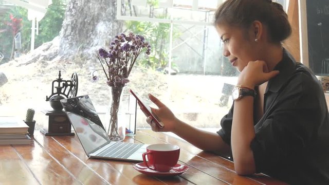 Happy Asian woman drinking coffee and work at café.