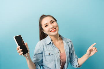Happy carefree young woman dancing and listening to music from smartphone over blue background