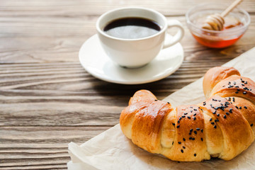 croissant, a cup of instant coffee and honey on a textured wooden background top view, cozy and delicious breakfast. Rustic background