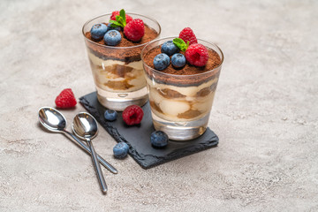Classic tiramisu dessert with blueberries and raspberries in a glass on stone serving board on concrete background