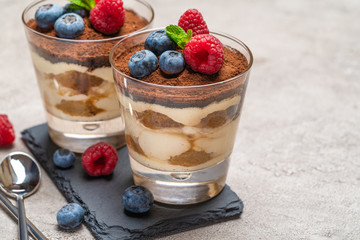 Classic tiramisu dessert with blueberries and raspberries in a glass on stone serving board on concrete background
