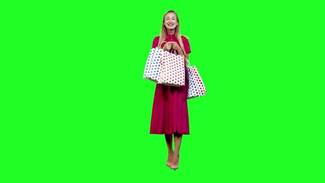 Stylish woman looking into her shopping bags and smiles while walking in full shot over green screen.