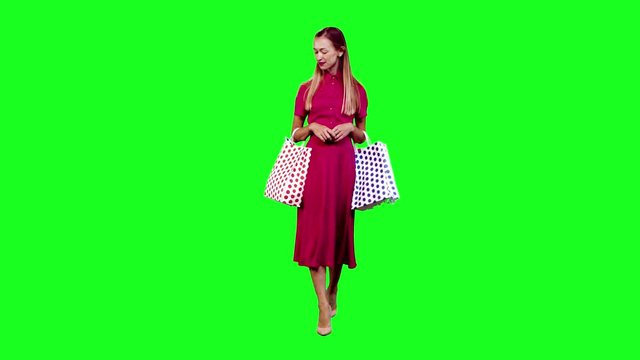 Stylish woman looking around and waving happily while walking in full shot over green screen.