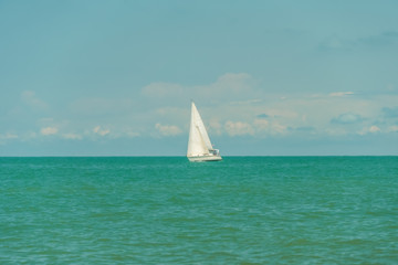 White sailing yacht in the black sea against the sky with clouds in sunny weather