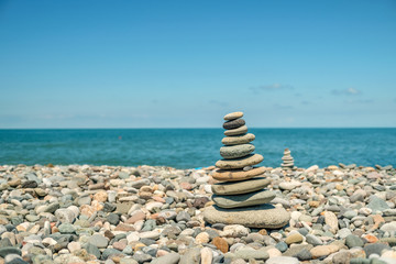 Cairn on a pebble beach against the background of the sea and the second cairn on a sunny day. Travel and Vacation Concept