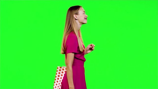 Stylish happy woman walks, smiles and waves "hello" to the camera in medium shot over green screen.