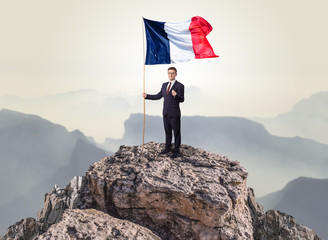 Obraz premium Successful businessman on the top of a mountain holding France victory flag