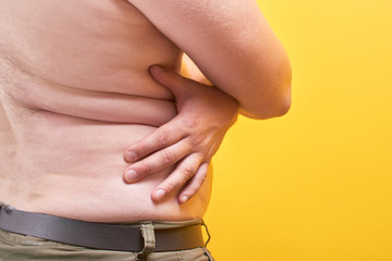 Man with naked body touches big fat belly on yellow background in studio closeup. Concept of...