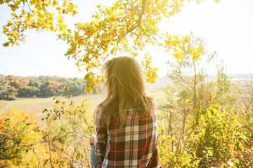Girl in the checkered shirt is sitting in the autumn forest. Seasonal concept. Stylish hipster...