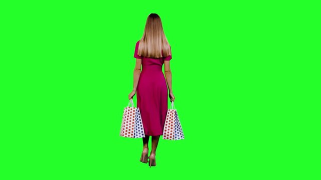 Walking away,  a beautiful stylish woman with shopping bags over green screen in long shot.