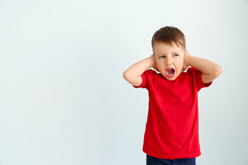 Screaming little boy with autistic disorder covering ears on light background