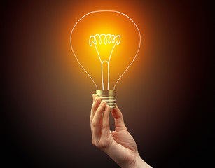 Hand holding light bulb on dark background, new idea concept