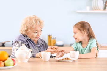 Cute little girl and grandmother drinking tea with cookies in kitchen