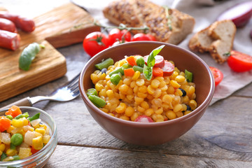 Bowl with tasty boiled legumes, vegetables and sausages on wooden table