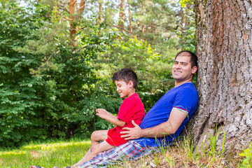 father and son resting under a tree in the summer