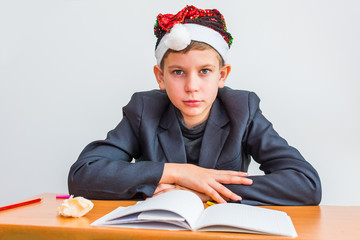 serious teenage boy in Santa's hat at the table with books