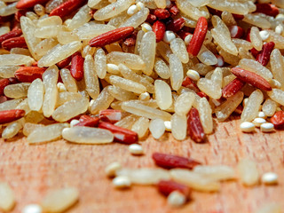 Mix red rice, complete rice, quinoa uncooked on wooden spoon and wooden surface 