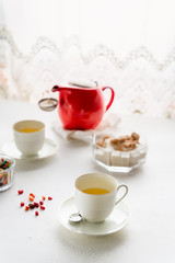 Obraz na płótnie Canvas Red tea pot, two white tea cups, sugar bowl on a table by window