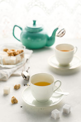 Fototapeta premium Teal colored tea pot, two white tea cups, sugar bowl on a table by window