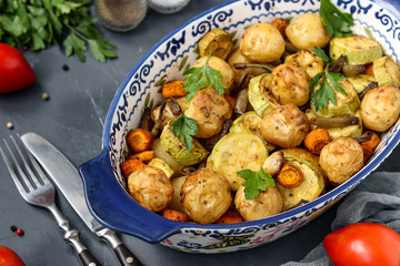 Young baked potato with zucchini, carrots and green beans, located in a ceramic form, against a dark background, horizontal orientation