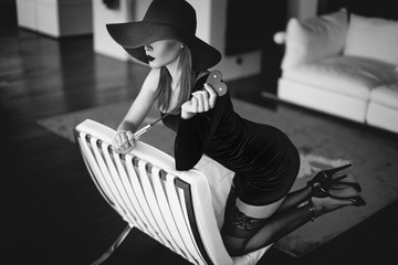 Sexy dominant femme fatale with whip kneeling on sofa black and white