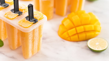 Fresh mango fruit popsicle ice in the plastic shaping box on bright marble table. Summer mood...