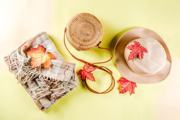 Multicolored autumn background. Women's felt hat, wicker bag, checkered plaid, autumn red yellow leaves. Yellow background, top view, wide composition. Autumn fashion, cozy fall concept, flatlay