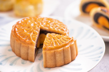 Mid-Autumn Festival traditional food concept - Beautiful cut moon cake on blue pattern plate on white background with flower, close up, copy space