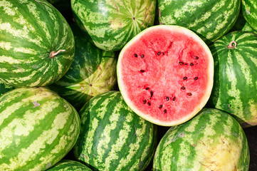 Red ripe watermelon cut in half on a pile of ripe watermelons in the field. A red cut watermelon view from above. - obrazy, fototapety, plakaty