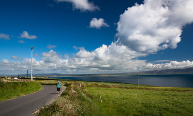 Fototapeta na wymiar senior woman walking on rural road on the west coast of County Kerry, Ireland, scenic landscape
