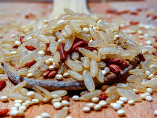 Mix red rice, complete rice, quinoa uncooked on wooden spoon and wooden surface 