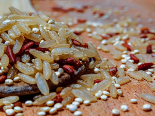 Mix red rice, complete rice, quinoa uncooked on wooden spoon and wooden surface 