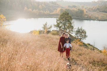 Fototapeta na wymiar Samesex caucasian lesbian family with a child and a dog walking outdoors on the background of beautiful nature. Mothers having fun with their son.
