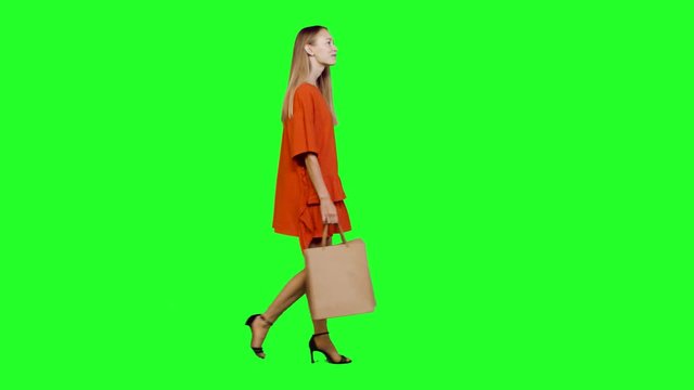 Happy woman with shopping bags walking and smiling over green screen in full body shot.
