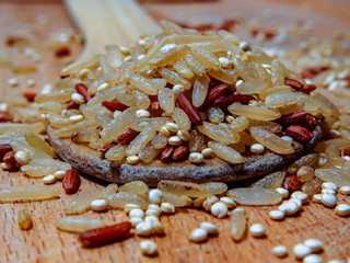 Mix red rice, complete rice, quinoa uncooked on wooden spoon and wooden surface 