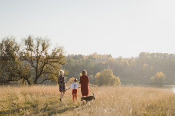 Naklejka premium Samesex caucasian lesbian family with a child and a dog walking outdoors on the background of beautiful nature. Mothers having fun with their son.