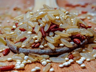 Mix red rice, complete rice, quinoa uncooked on wooden spoon and wooden surface 