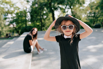 Stylish little girl wearing sunglasses and black dress posing at camera with lovely smile with...