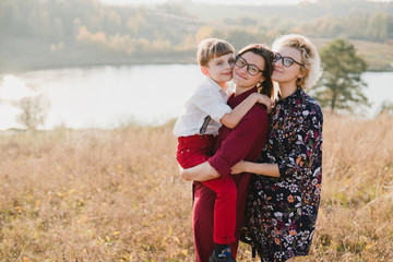 Samesex caucasian lesbian family with a child and a dog walking outdoors on the background of beautiful nature. Mothers having fun with their son.