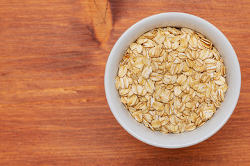 Raw bulgur in a white bowl on brown background.