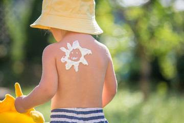 Toddler child with suntan lotion shaped as sun on his back, going at the beach with toys and flufy...