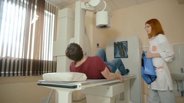 Patient man lies on the bed, x-ray examination. Female doctor prepares an x-ray machine for work