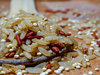 Mix red rice, complete rice, quinoa uncooked on wooden spoon and wooden surface 