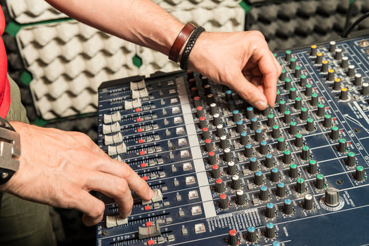 Detail of the hands of a man manipulating a mixing desk.
